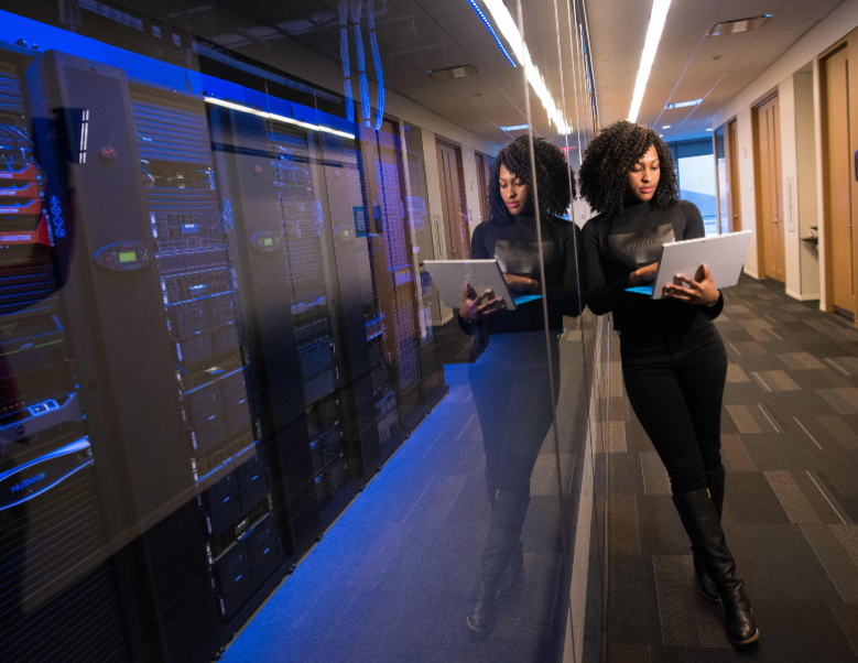 Woman standing with laptop in front of computer board wall